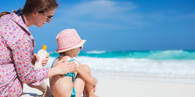 Mutter cremt Kind mit Sonnencreme am Strand ein
